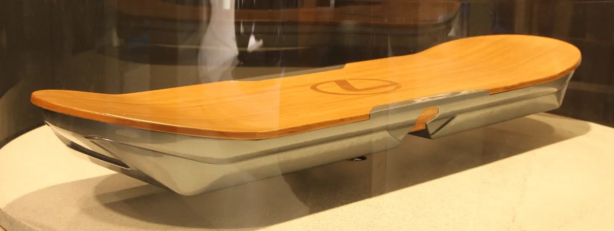 A Lexus Hoverboard mockup in a glass display case, with a wooden skateboard-style deck and a silver underside housing