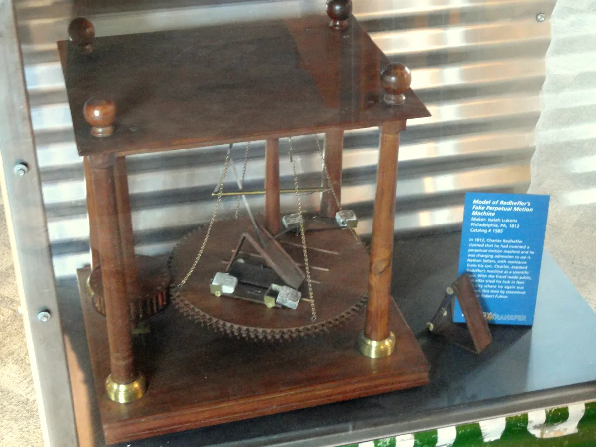A wooden model of Charles Redheffer's perpetual motion machine in a museum case, with a toothed wheel, brass fittings and an exhibit label