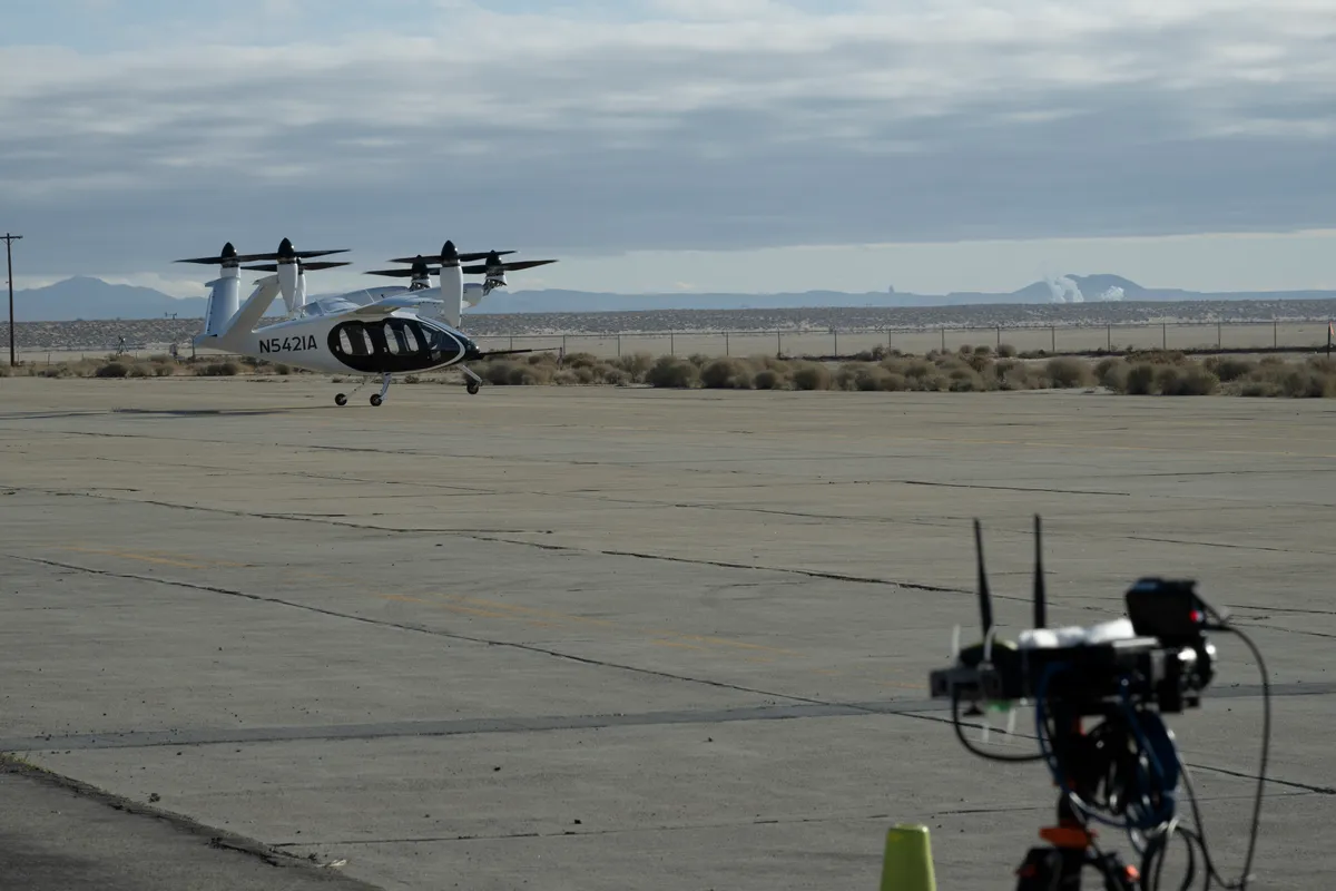 A white Joby air taxi on a concrete ramp at Edwards, California, with a NASA sensor box with two antennas on a tripod in the foreground