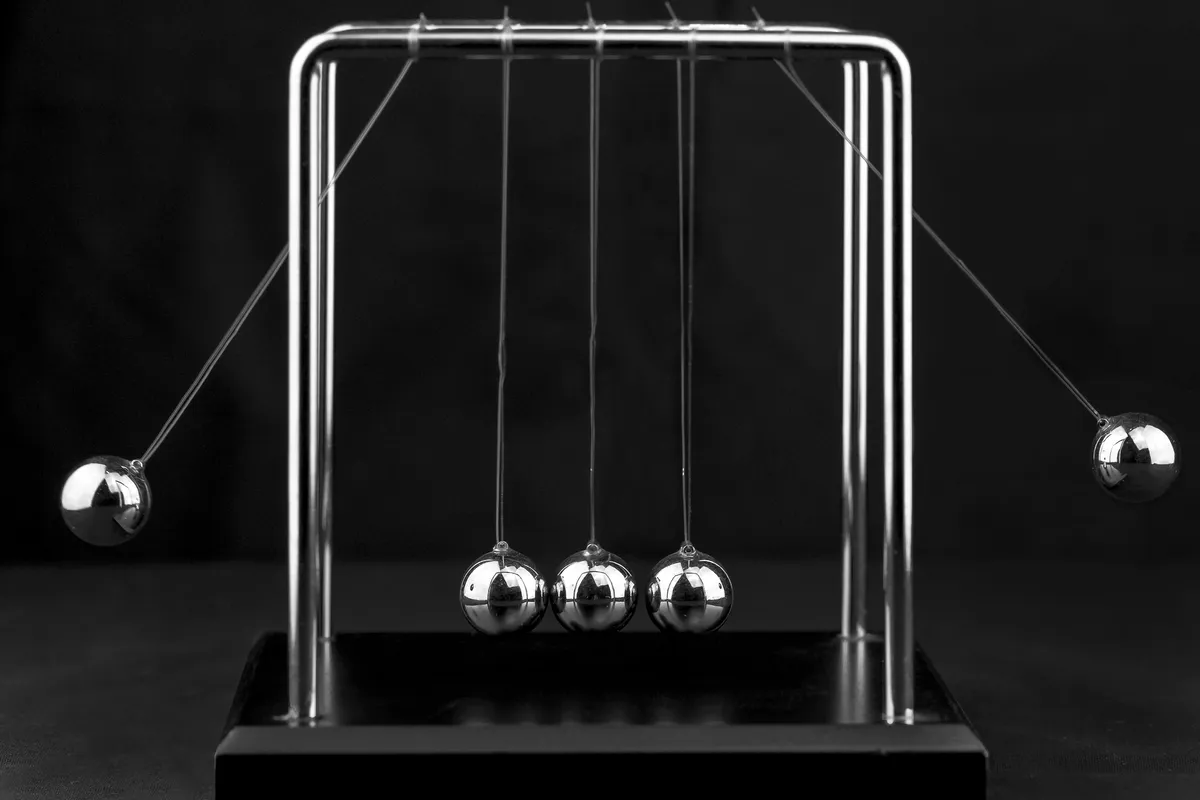 A Newton's cradle on a black background with two steel balls pulled out to the sides and three balls hanging in the middle