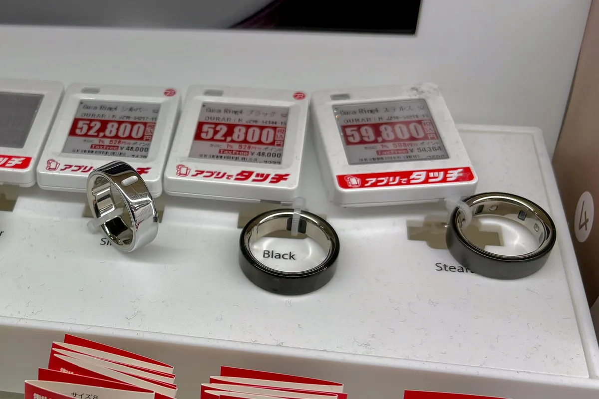 Silver, black and dark grey Oura Ring 4 smart rings on a white store display stand, each in front of an electronic price tag