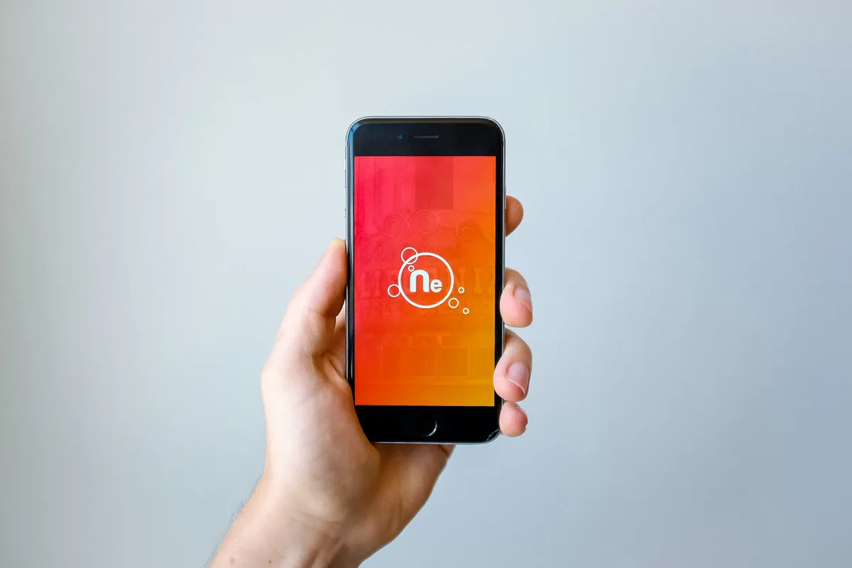 A hand holding a smartphone with a bright orange screen against a pale gray wall